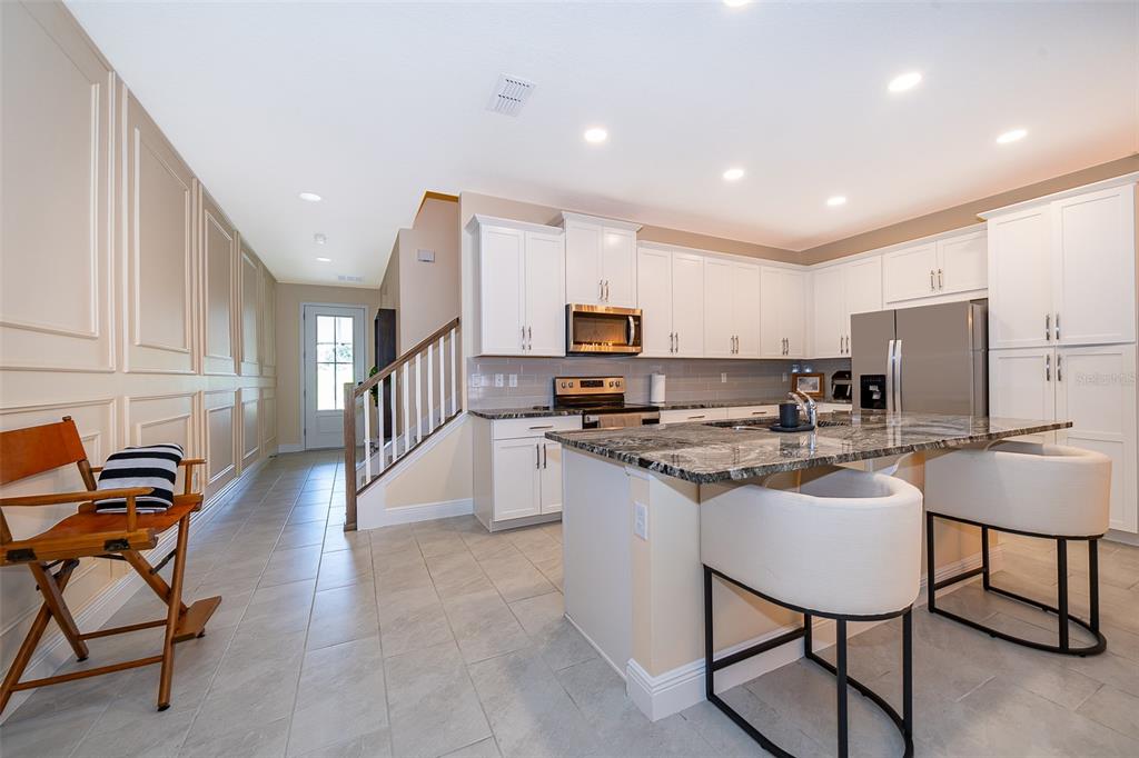 A modern kitchen features white cabinetry, a granite-topped island with bar stools, and tiled flooring — 1660 TROPICAL PALMS CIRCLE, KISSIMMEE, FL