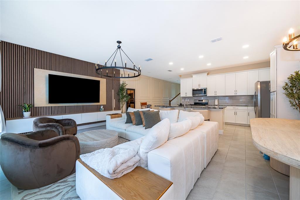 An open-concept living room and kitchen featuring a slatted wood accent wall and white cabinetry — 1660 TROPICAL PALMS CIRCLE, KISSIMMEE, FL