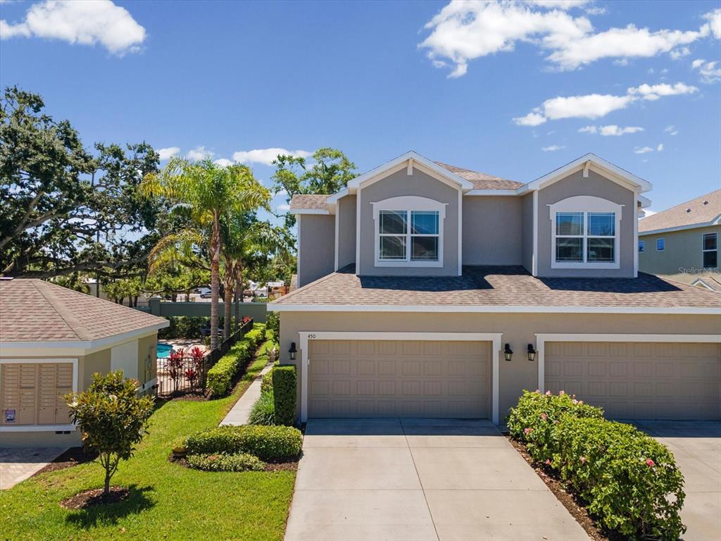 A two-story townhouse features a beige exterior, a two-car garage, and a concrete driveway — 450 HARBOR SPRINGS DRIVE, PALM HARBOR, FL