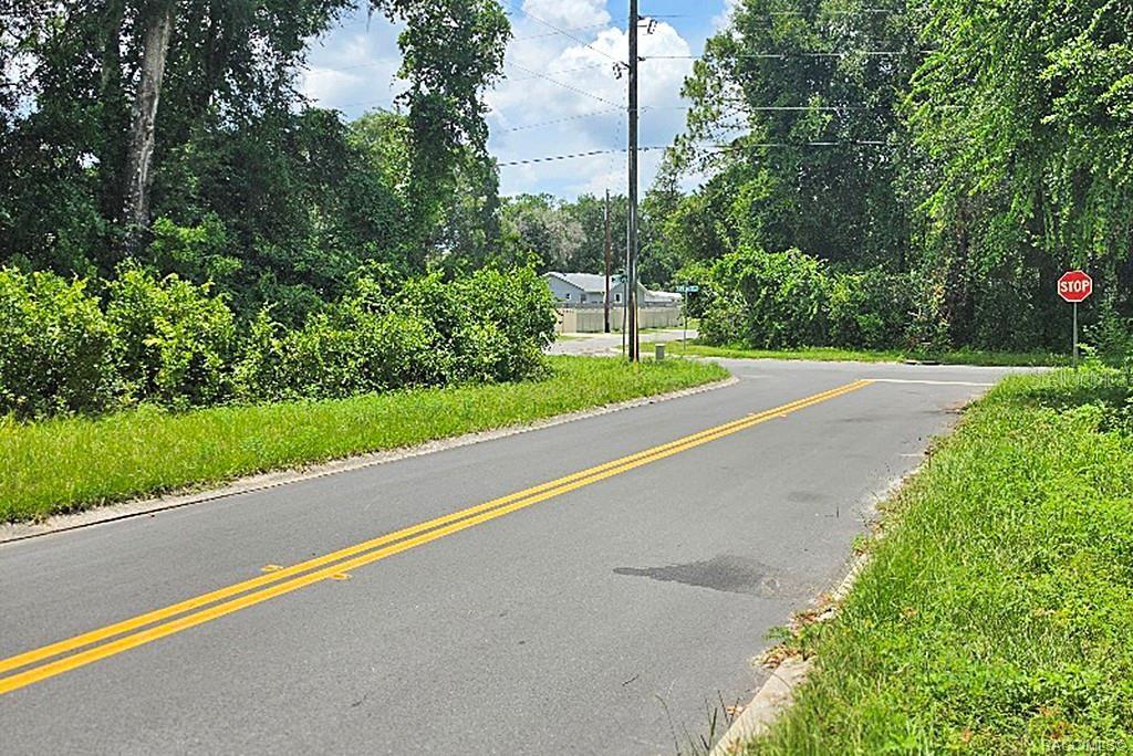 A paved road with double yellow lines leads toward a stop sign and trees — 1606 CALDWELL STREET, INVERNESS, FL