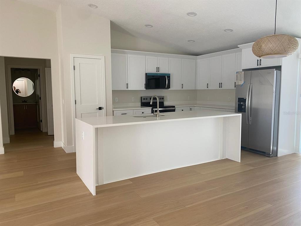 A modern kitchen features white cabinets, a large quartz island, and light wood flooring — 895 S CEDAR AVENUE, ORANGE CITY, FL