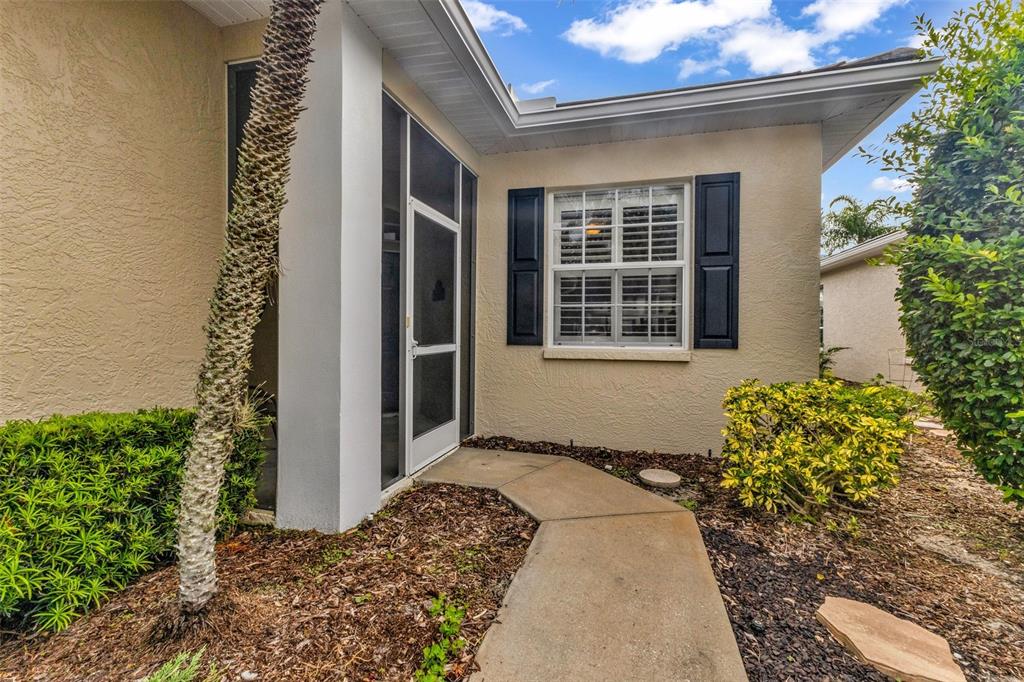 A concrete walkway leads to a screened entryway and a window with black shutters — 834 MONTROSE DRIVE UNIT 9, VENICE, FL