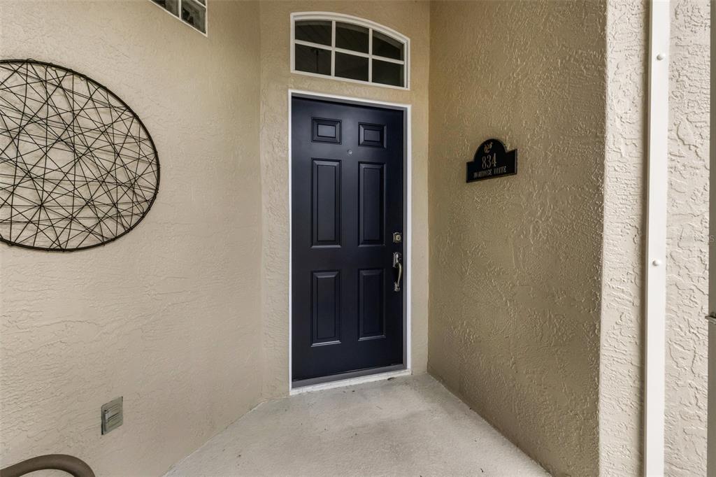 A dark blue front door with a transom window sits on a beige stucco porch — 834 MONTROSE DRIVE UNIT 9, VENICE, FL