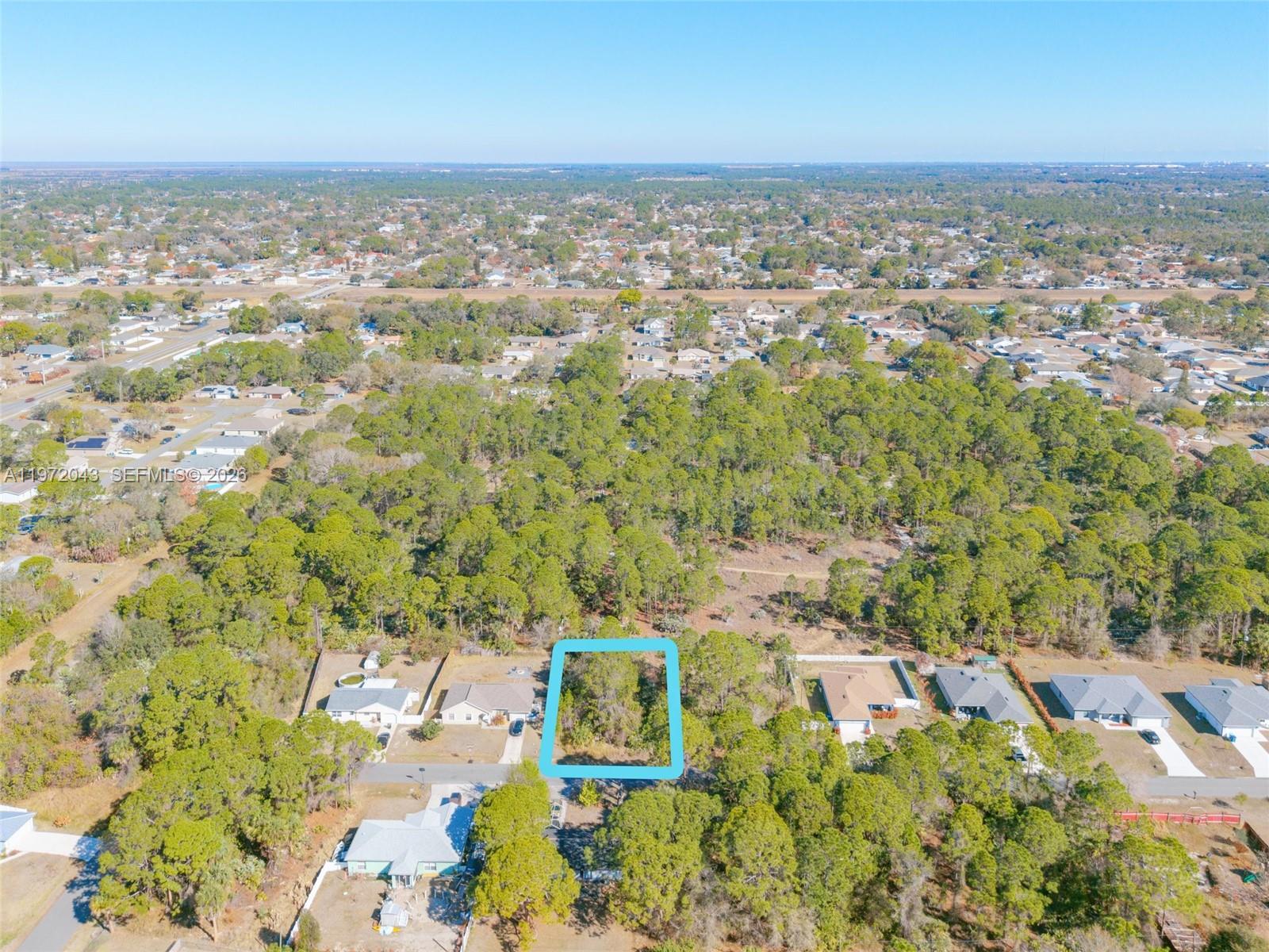 An aerial view shows a vacant, rectangular residential lot outlined in blue amidst a wooded neighborhood — 825 Doverbrook Rd NW, Palm Bay FL 32907, PALM BAY, FL