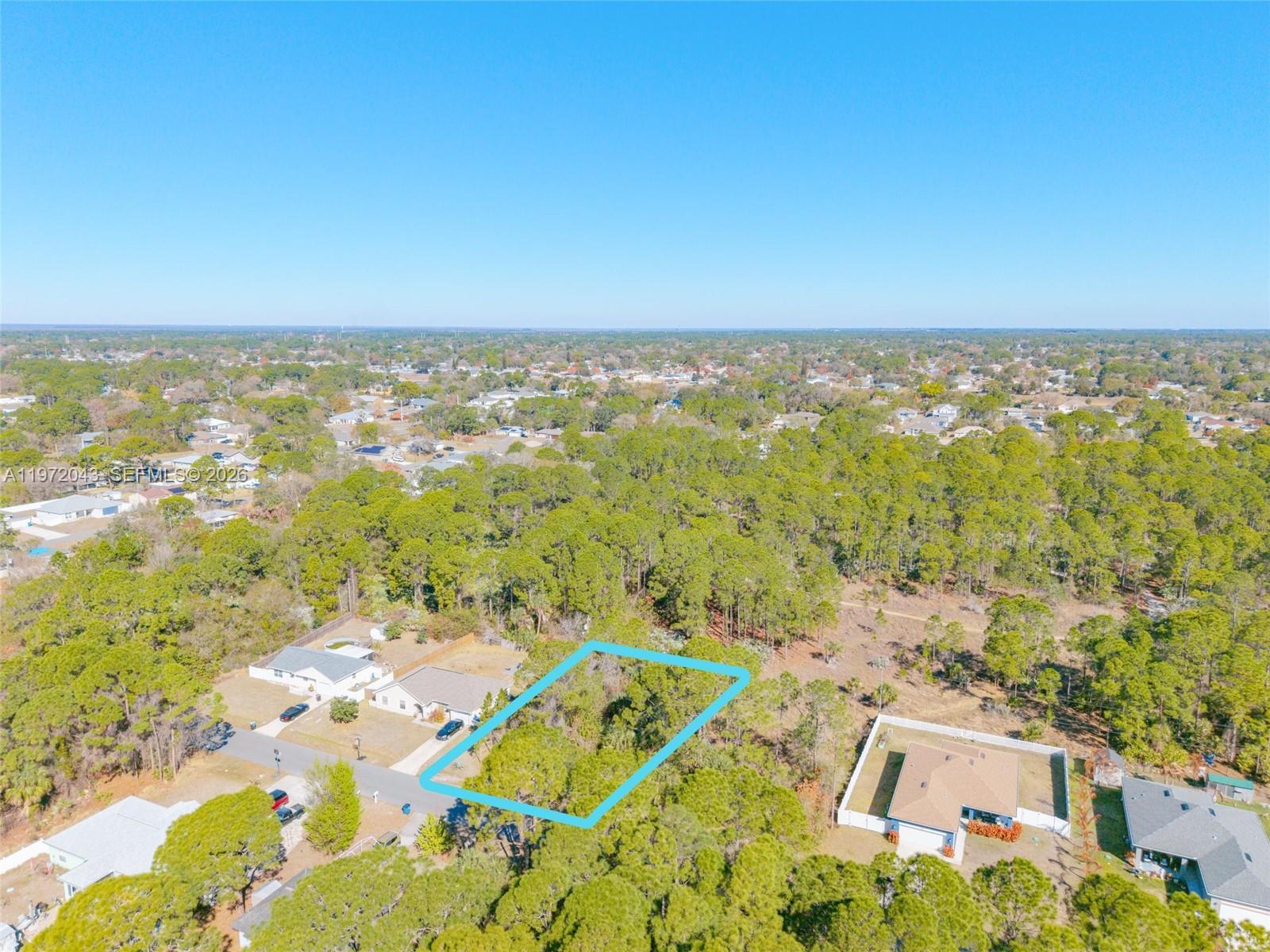 An aerial view shows a vacant, rectangular residential lot outlined in blue amidst a wooded neighborhood — 825 Doverbrook Rd NW, Palm Bay FL 32907, PALM BAY, FL