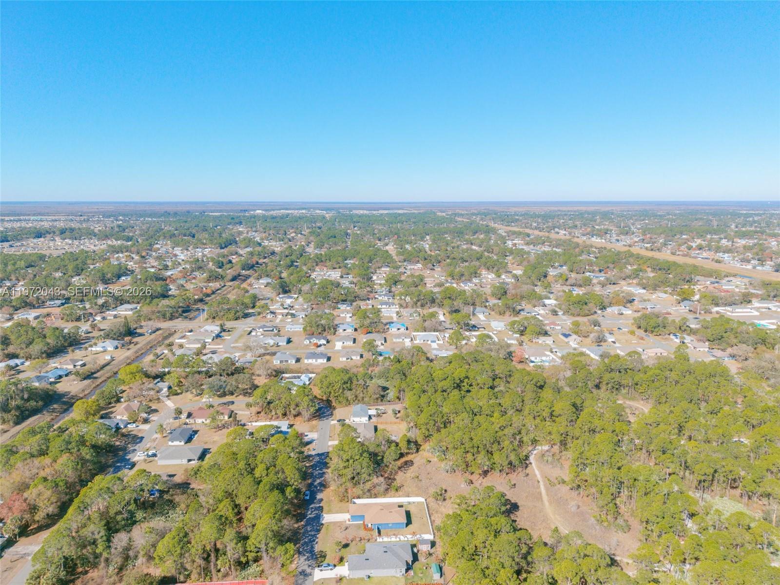 An aerial view shows a suburban neighborhood with houses interspersed among dense green trees — 825 Doverbrook Rd NW, Palm Bay FL 32907, PALM BAY, FL