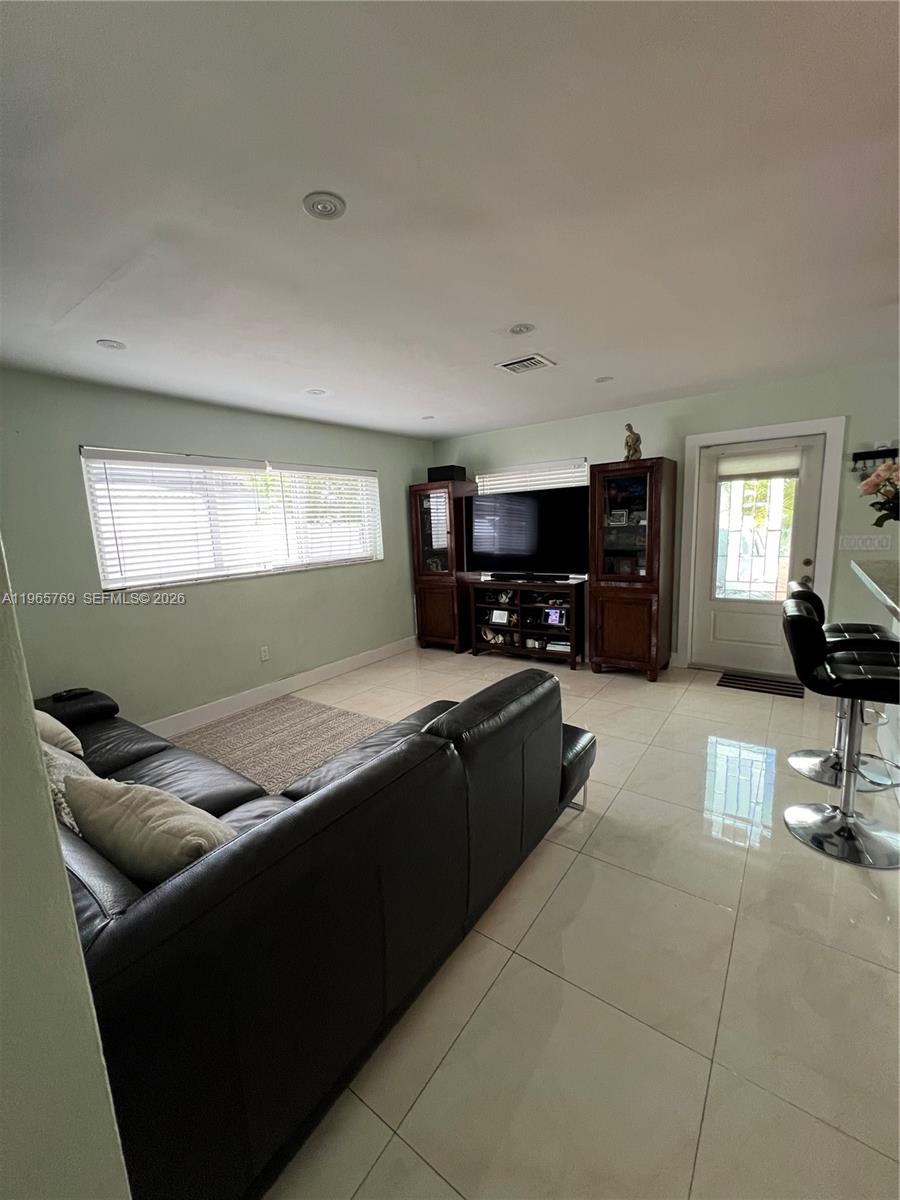 A living room features a black leather sectional, a television console, and light tile flooring — 10382 SW 25th St, Miami FL 33165, MIAMI, FL