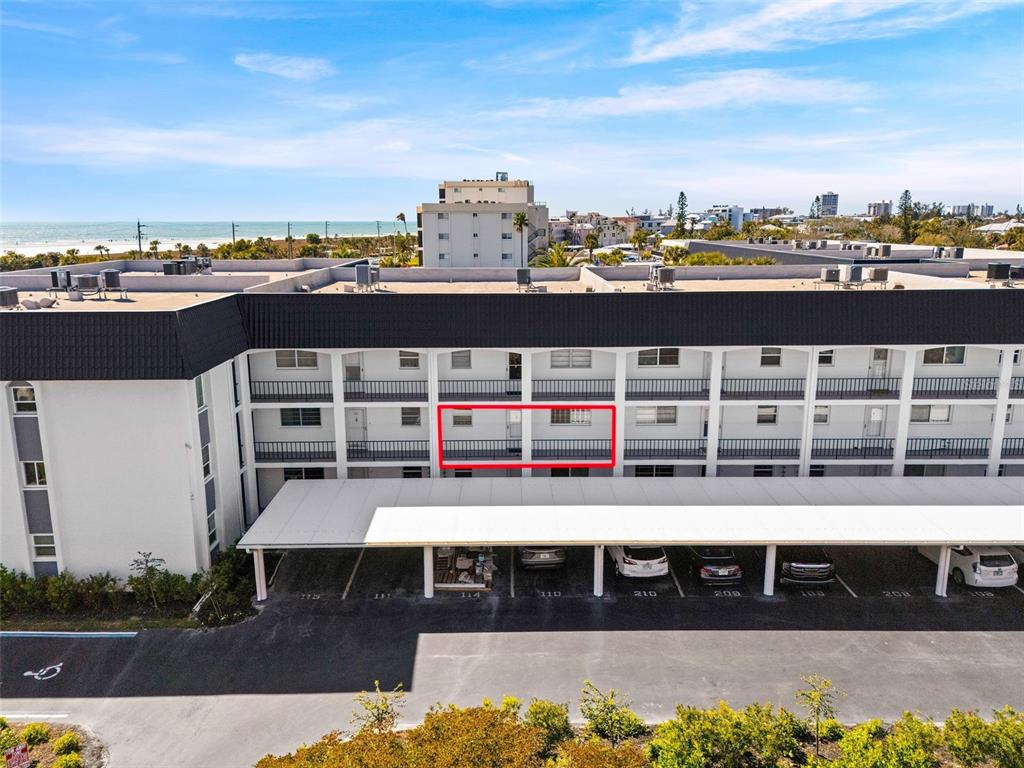 An exterior view of a multi-story apartment building with a covered parking area below — 5600 BEACH WAY DRIVE UNIT 210, SARASOTA, FL
