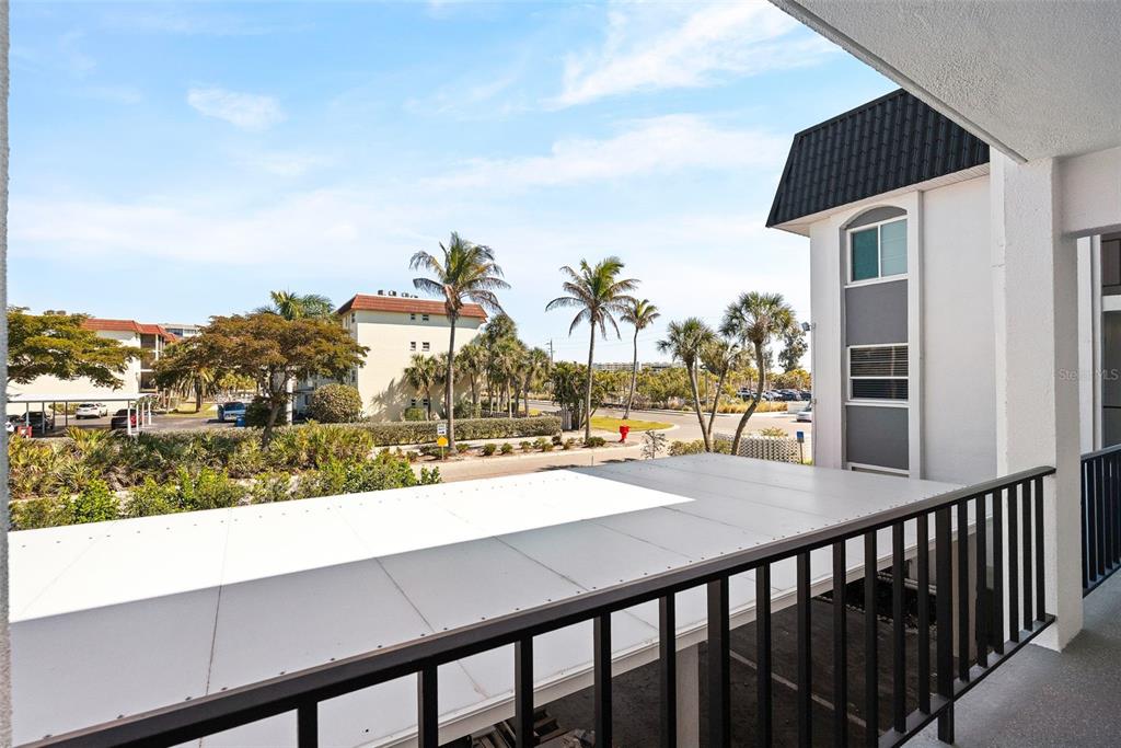 A view from a balcony overlooking a parking area, palm trees, and neighboring apartment buildings — 5600 BEACH WAY DRIVE UNIT 210, SARASOTA, FL