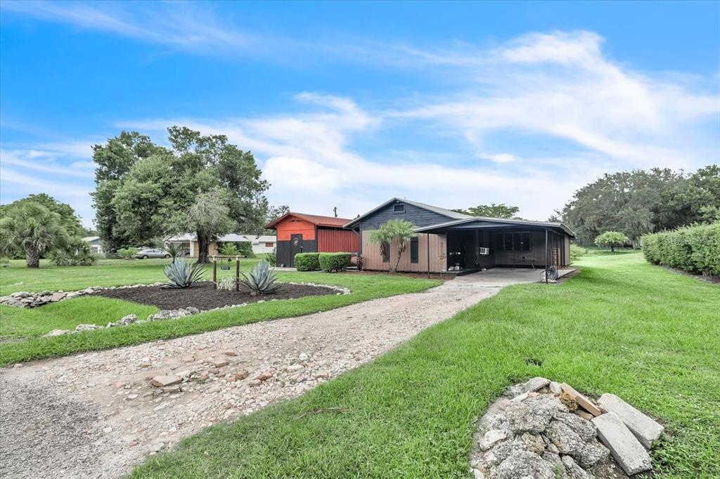 A gravel driveway leads to a one-story house with a carport and a red shed — 915 E CHARLES STREET, ARCADIA, FL