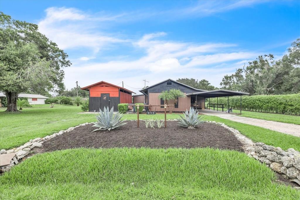 A house with a carport and a red shed sits behind a landscaped front yard — 915 E CHARLES STREET, ARCADIA, FL