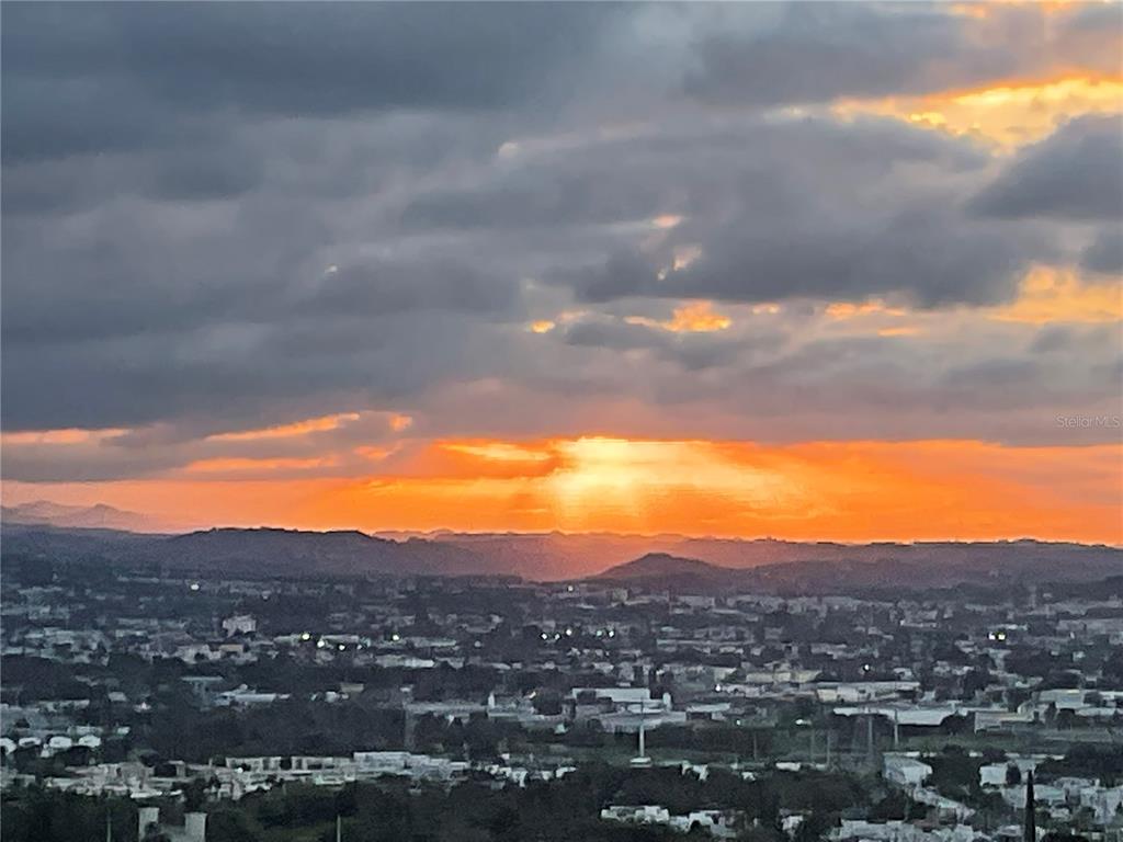 A scenic view of a city landscape beneath a dramatic sunset with cloudy skies — Carretera 833 PLAZA DEL PRADO UNIT 1304, GUAYNABO, PR