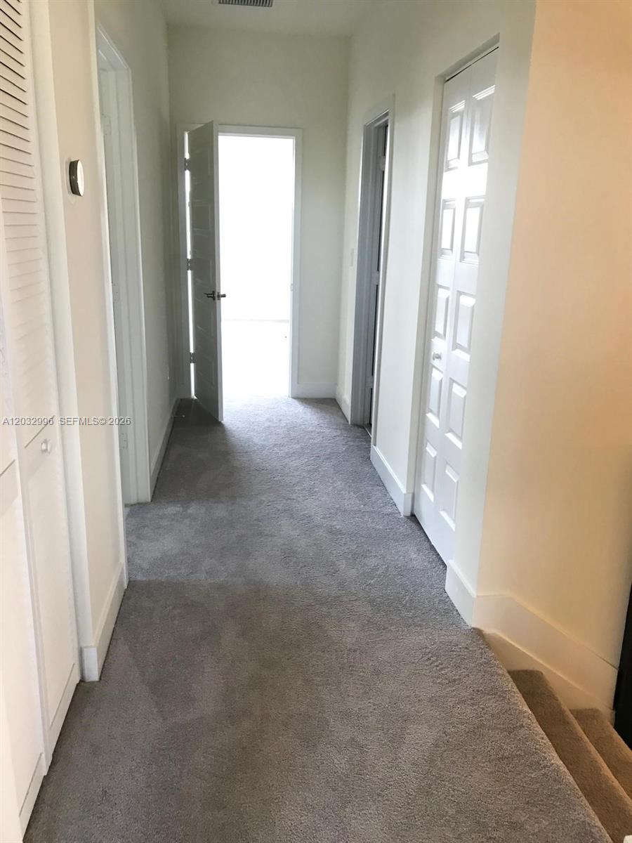 A carpeted hallway features white walls, multiple closed doors, and an open doorway at the end — 8102 NW 105th Ct # 8102, Doral FL 33178, DORAL, FL