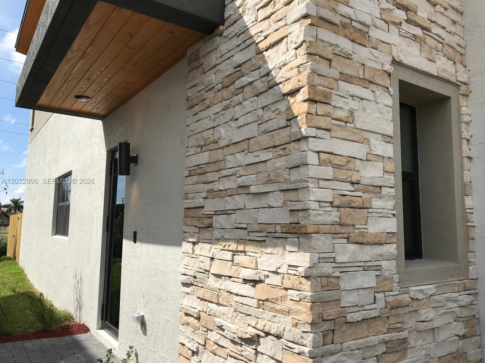 A modern home exterior features a stone-clad corner, stucco walls, and a wood-paneled entryway ceiling — 8102 NW 105th Ct # 8102, Doral FL 33178, DORAL, FL