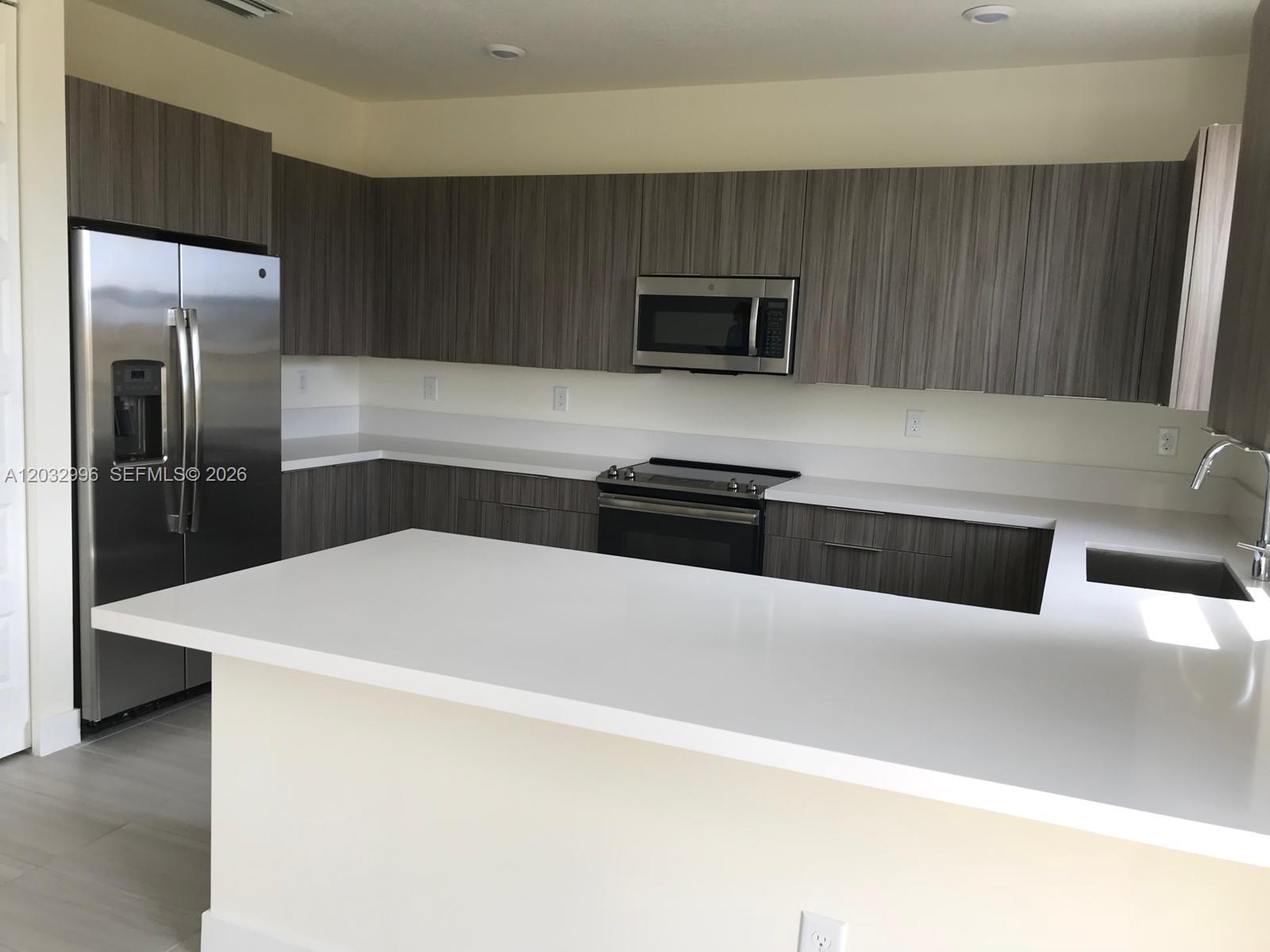 A modern kitchen features dark wood-grain cabinets, white countertops, and stainless steel appliances — 8102 NW 105th Ct # 8102, Doral FL 33178, DORAL, FL