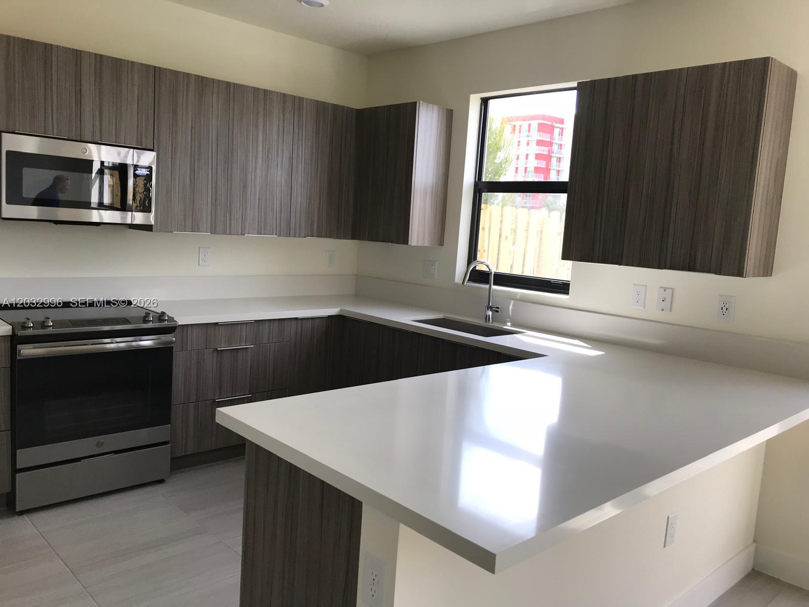 A modern kitchen features dark wood-grain cabinets, white countertops, stainless steel appliances, and a window — 8102 NW 105th Ct # 8102, Doral FL 33178, DORAL, FL