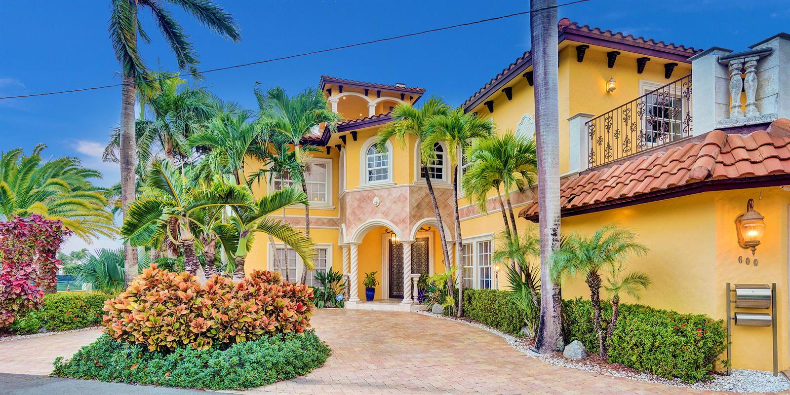 A yellow two-story Mediterranean-style house with a paved driveway and lush tropical landscaping — 600 Circle Drive, Pompano Beach FL 33062, POMPANO BEACH, FL