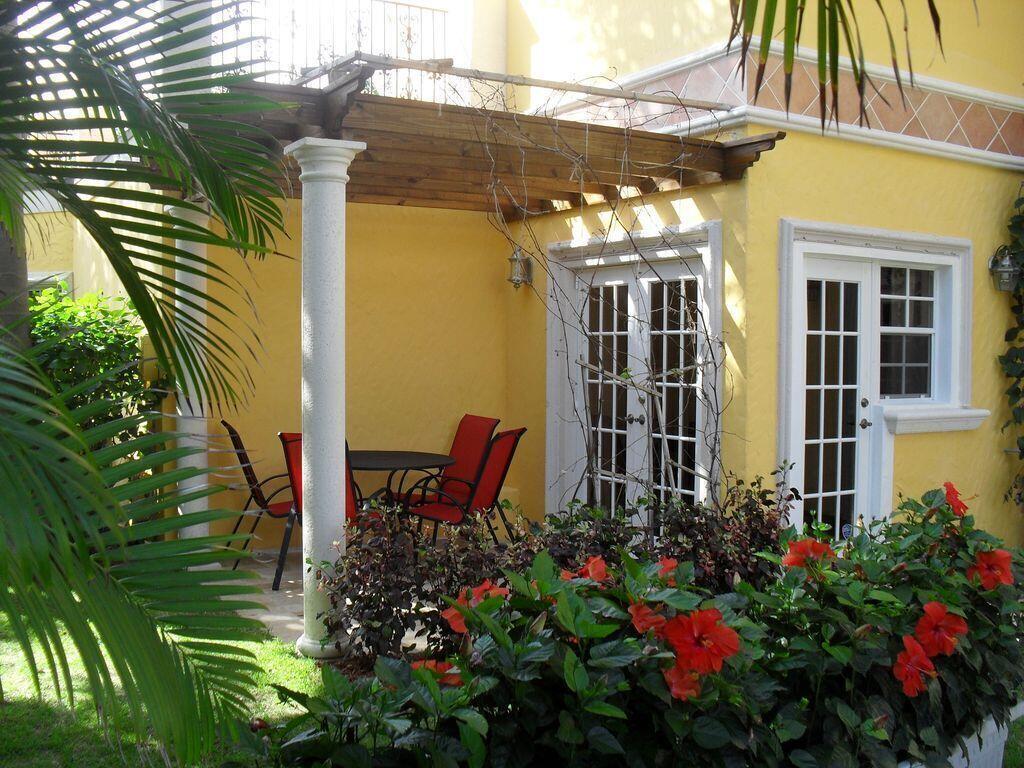 A yellow stucco patio features a wooden pergola, white columns, and red outdoor furniture — 600 Circle Drive, Pompano Beach FL 33062, POMPANO BEACH, FL