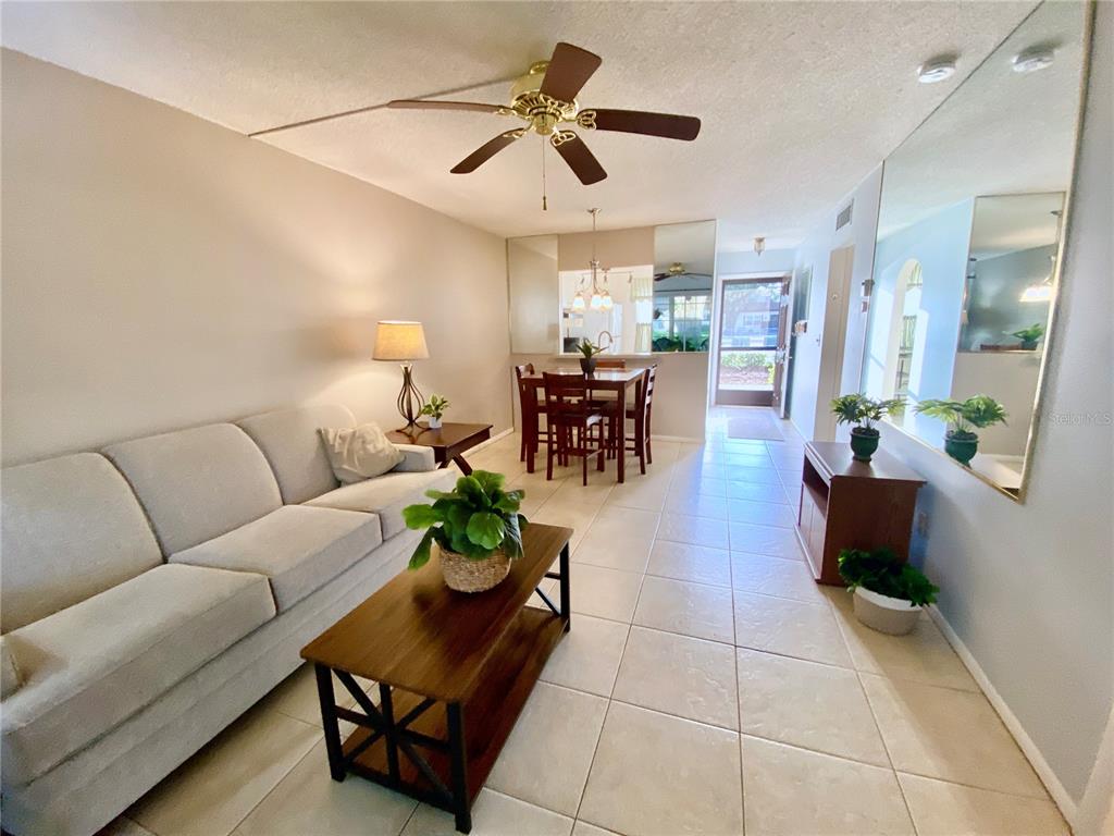 A screened-in porch with tiled flooring, four green plastic chairs, and a hanging plant — 3157 MISSION GROVE DRIVE, PALM HARBOR, FL