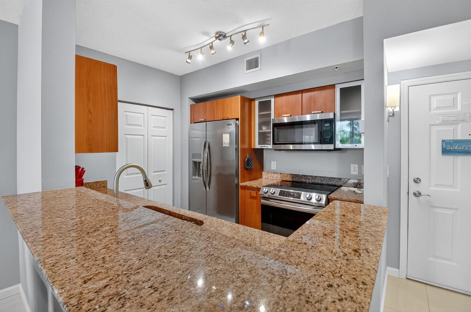 A kitchen features granite countertops, stainless steel appliances, and wood cabinetry against light gray walls — 625 Casa Loma Boulevard # 306, Boynton Beach FL 33435, BOYNTON BEACH, FL