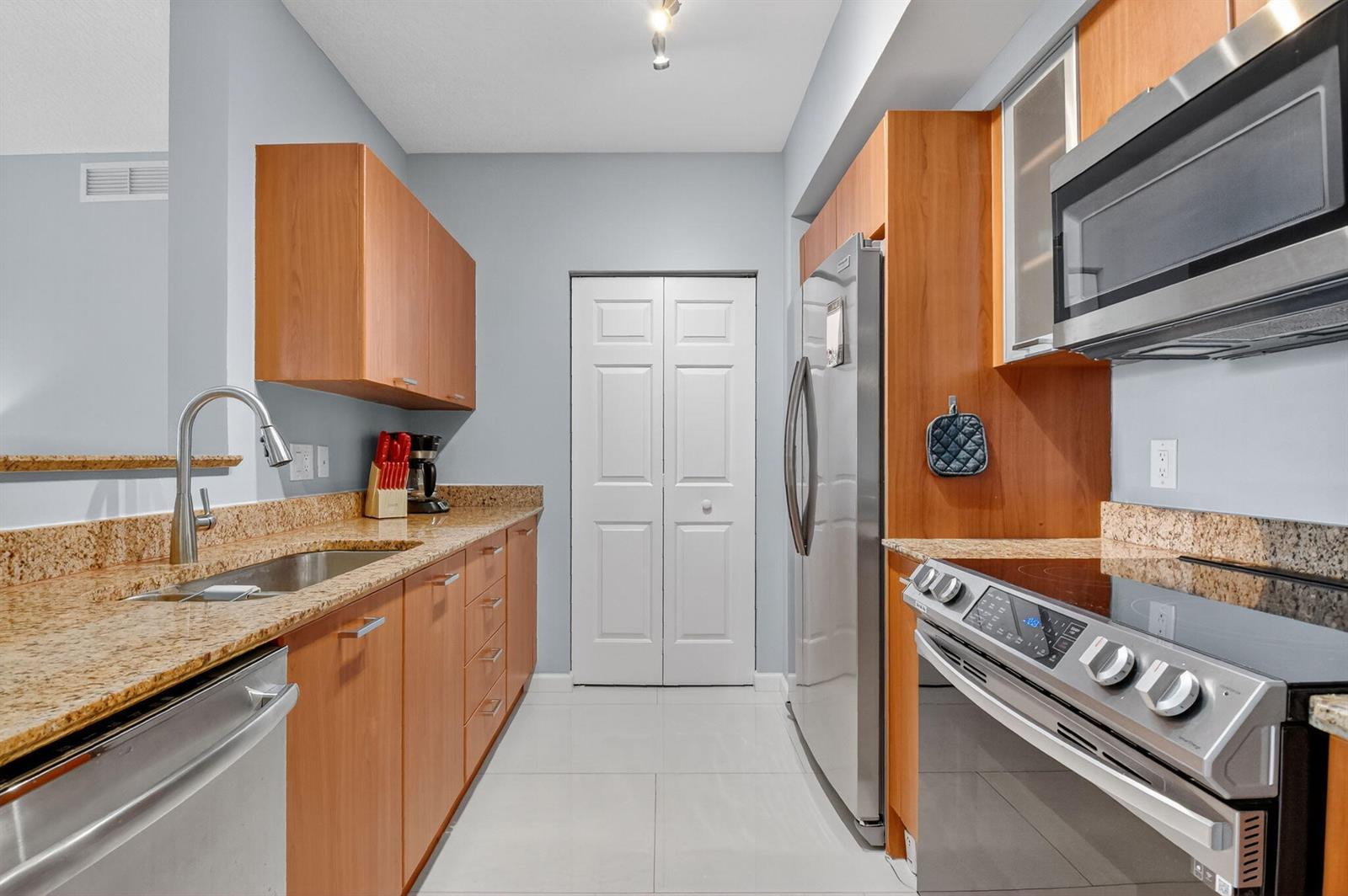 A galley kitchen features wood cabinets, granite countertops, stainless steel appliances, and light tile flooring — 625 Casa Loma Boulevard # 306, Boynton Beach FL 33435, BOYNTON BEACH, FL