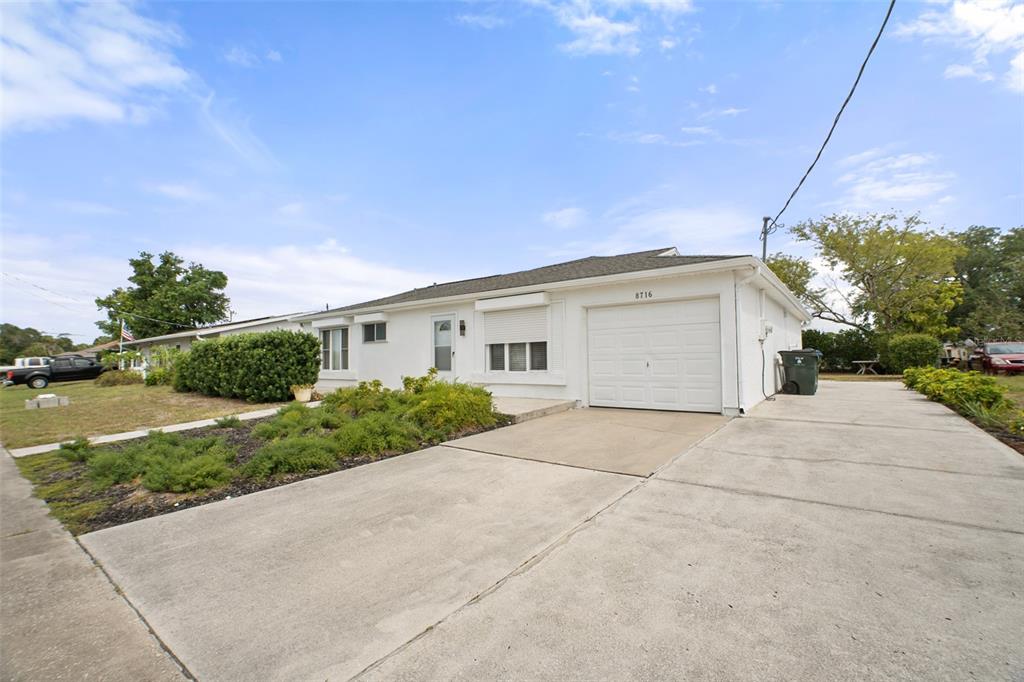 A white single-story house features a concrete driveway, a garage, and a landscaped front yard — 8716 TRIONFO AVENUE, NORTH PORT, FL