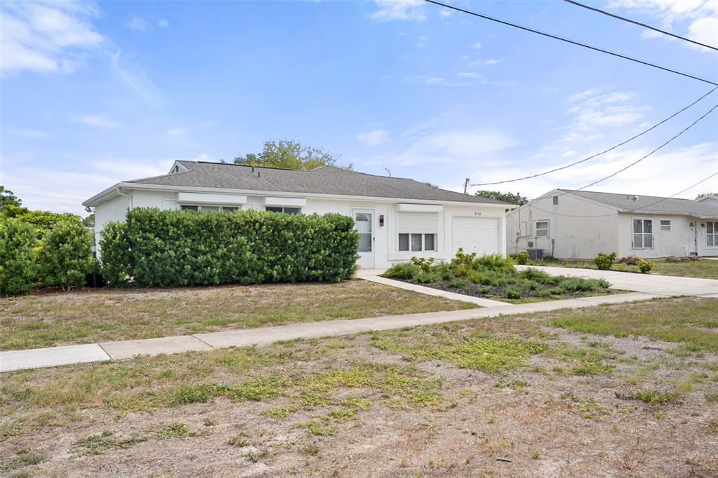 A single-story house with a white exterior, a garage, and a large hedge in front — 8716 TRIONFO AVENUE, NORTH PORT, FL