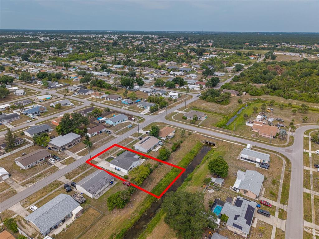 An aerial view shows a single-story house with a red-outlined lot bordering a drainage canal — 8716 TRIONFO AVENUE, NORTH PORT, FL