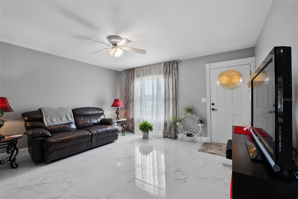 A living room features a dark leather sofa, white marble-look tile floors, and a television — 8716 TRIONFO AVENUE, NORTH PORT, FL