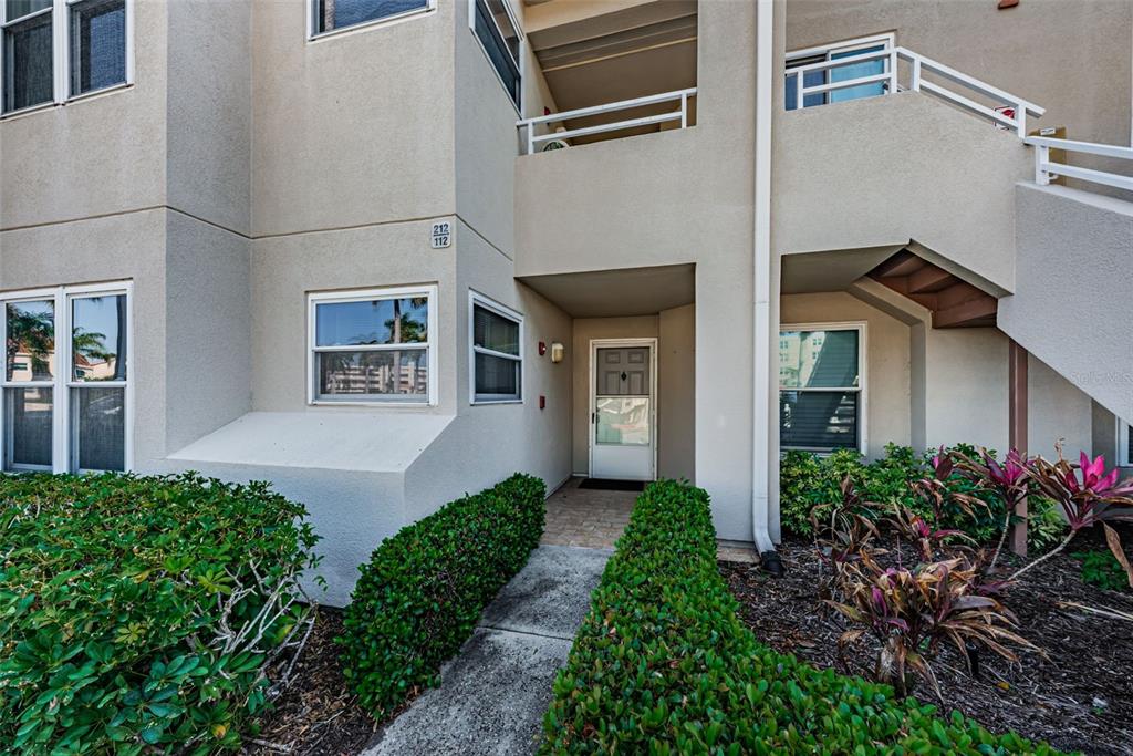 A beige multi-story building exterior features a ground-level entrance, stairs, and manicured landscaping — 6080 BAHIA DEL MAR CIRCLE UNIT 112, ST PETERSBURG, FL