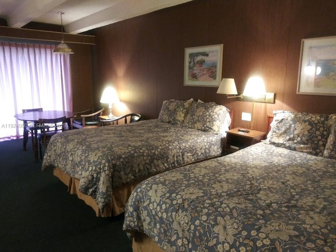 A hotel room features two beds with floral bedding, a small dining table, and wall-mounted lamps — 1001 LAKEVIEW DRIVE, Sebring FL 33870, SEBRING, FL