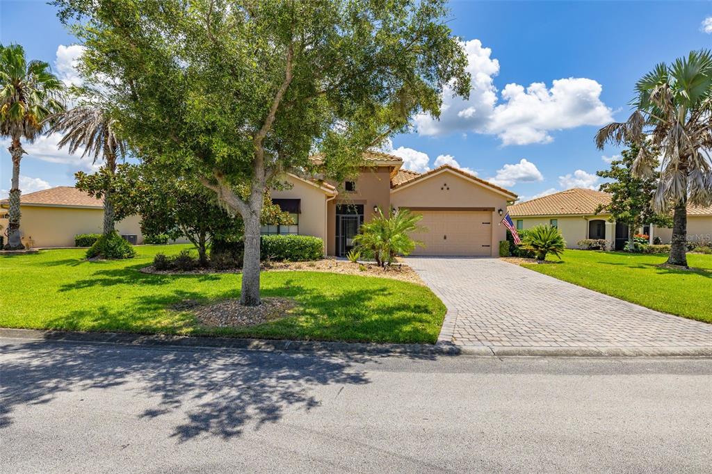 A single-story house with a tan stucco exterior, a paved driveway, and a large tree — 394 MONTEREY STREET, KISSIMMEE, FL