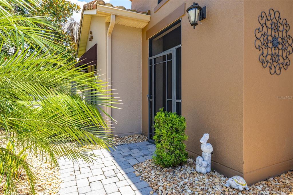 A paved walkway leads to a tan house entrance with a screen door and landscaping — 394 MONTEREY STREET, KISSIMMEE, FL