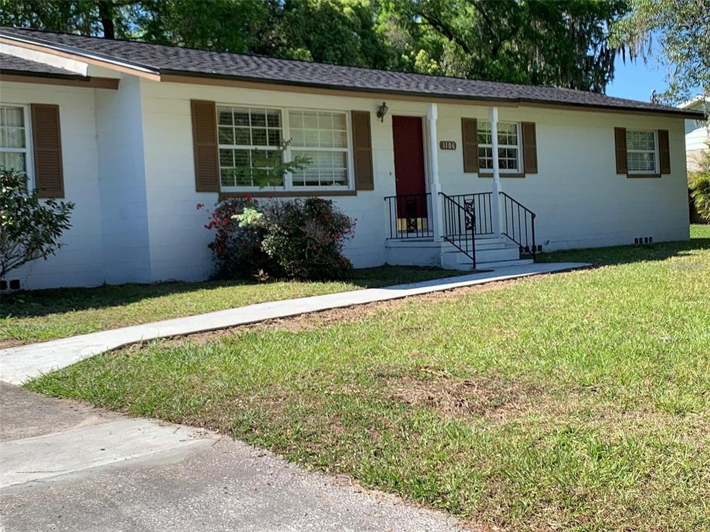 A white single-story house with brown shutters, a red front door, and a concrete walkway — 1106 NE 17TH TERRACE, OCALA, FL