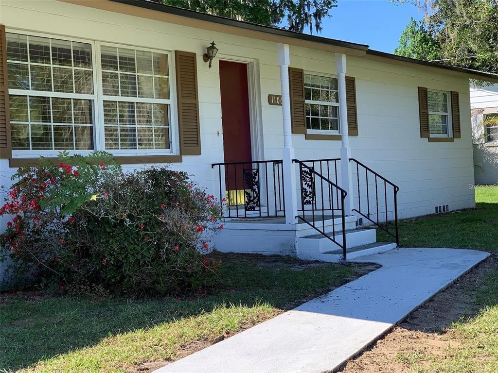 A white single-story house with brown shutters, a red front door, and a concrete walkway — 1106 NE 17TH TERRACE, OCALA, FL
