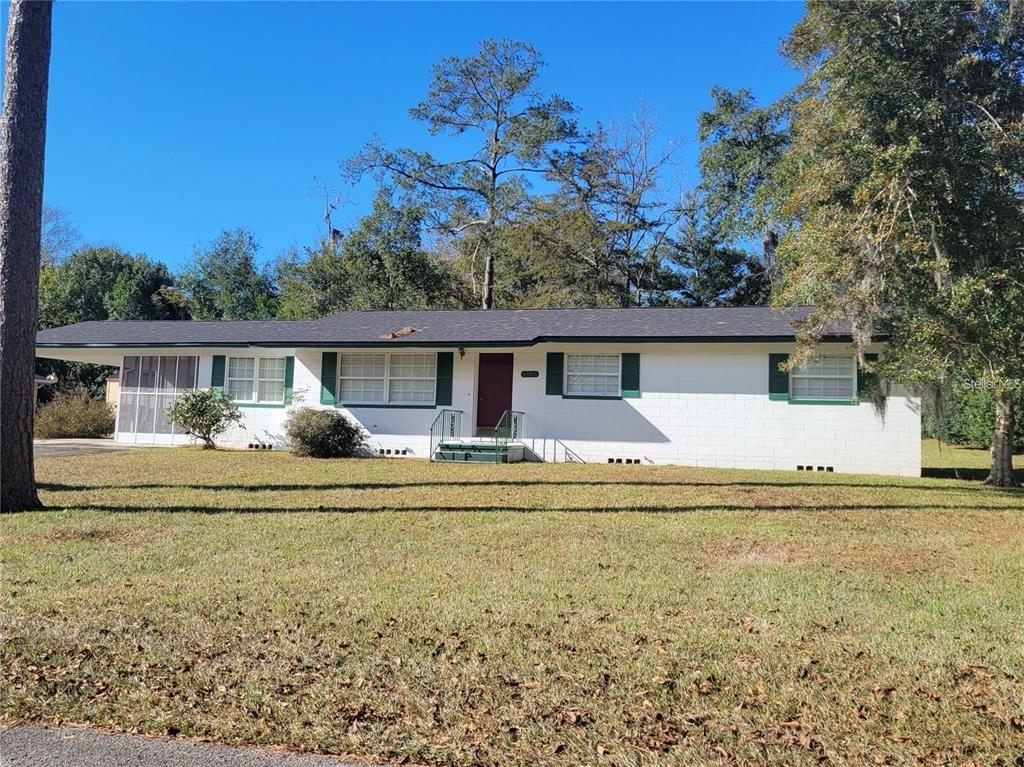 A single-story white brick house with a dark roof and green shutters sits on grass — 1106 NE 17TH TERRACE, OCALA, FL