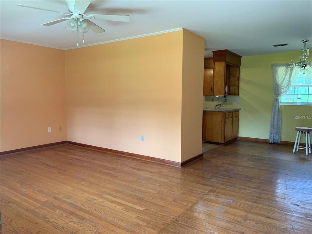 An interior view shows a living area with hardwood floors and a kitchen beyond — 1106 NE 17TH TERRACE, OCALA, FL