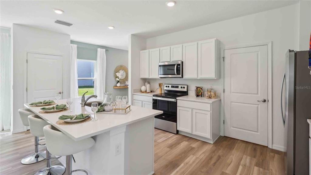 A modern kitchen features white cabinets, stainless steel appliances, and a large quartz island — 10582 TUCKER ROAD, WEEKI WACHEE, FL