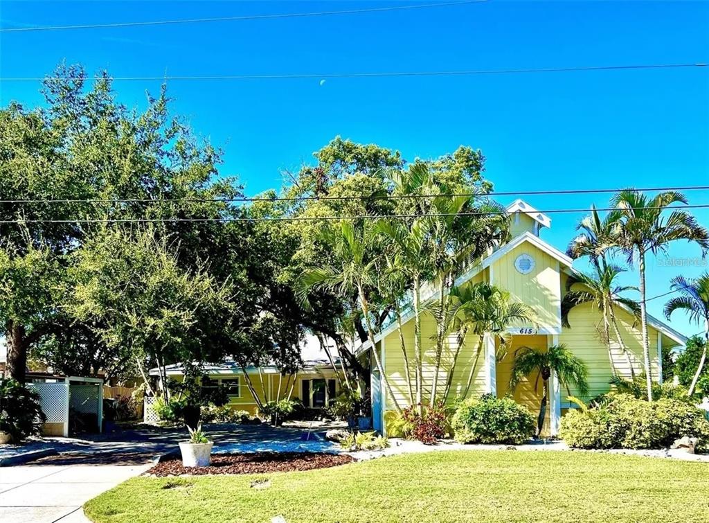A yellow house with a gabled roof is surrounded by palm trees and green landscaping — 615 N MAYO STREET, CRYSTAL BEACH, FL
