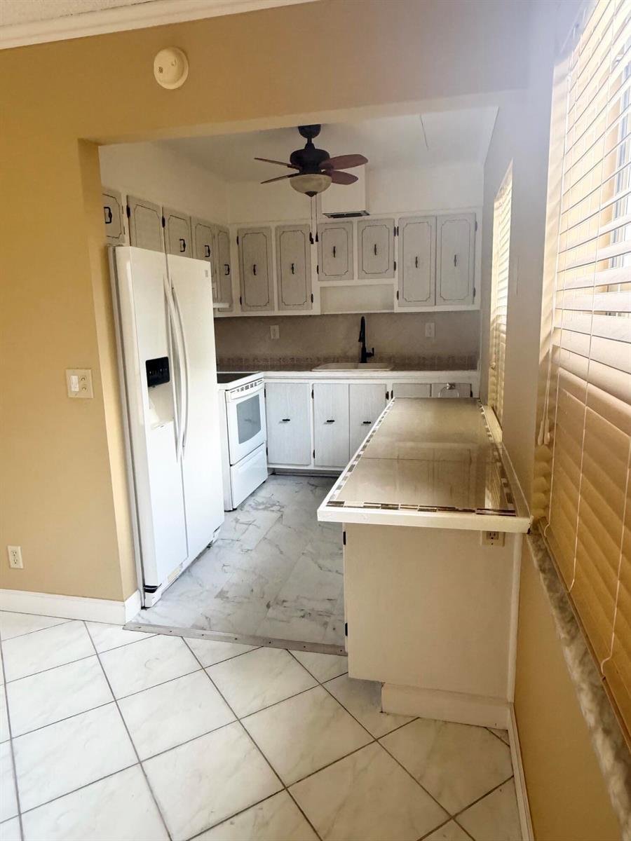 A kitchen features white cabinets, a white refrigerator, a stove, and a tiled breakfast bar — 814 Burgundy Q, Delray Beach FL 33484, DELRAY BEACH, FL