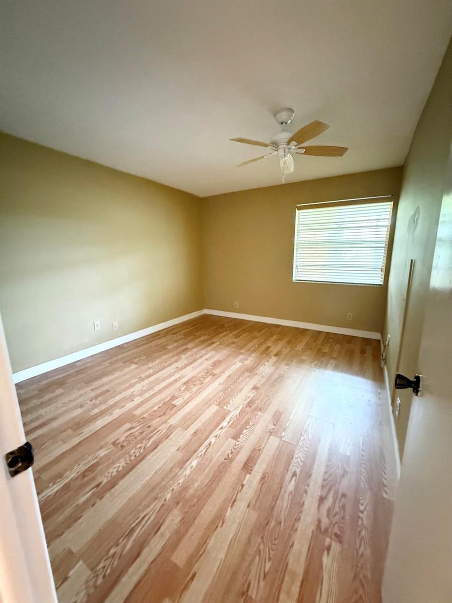 An empty bedroom features light-colored wood-look flooring, tan walls, and a ceiling fan — 814 Burgundy Q, Delray Beach FL 33484, DELRAY BEACH, FL