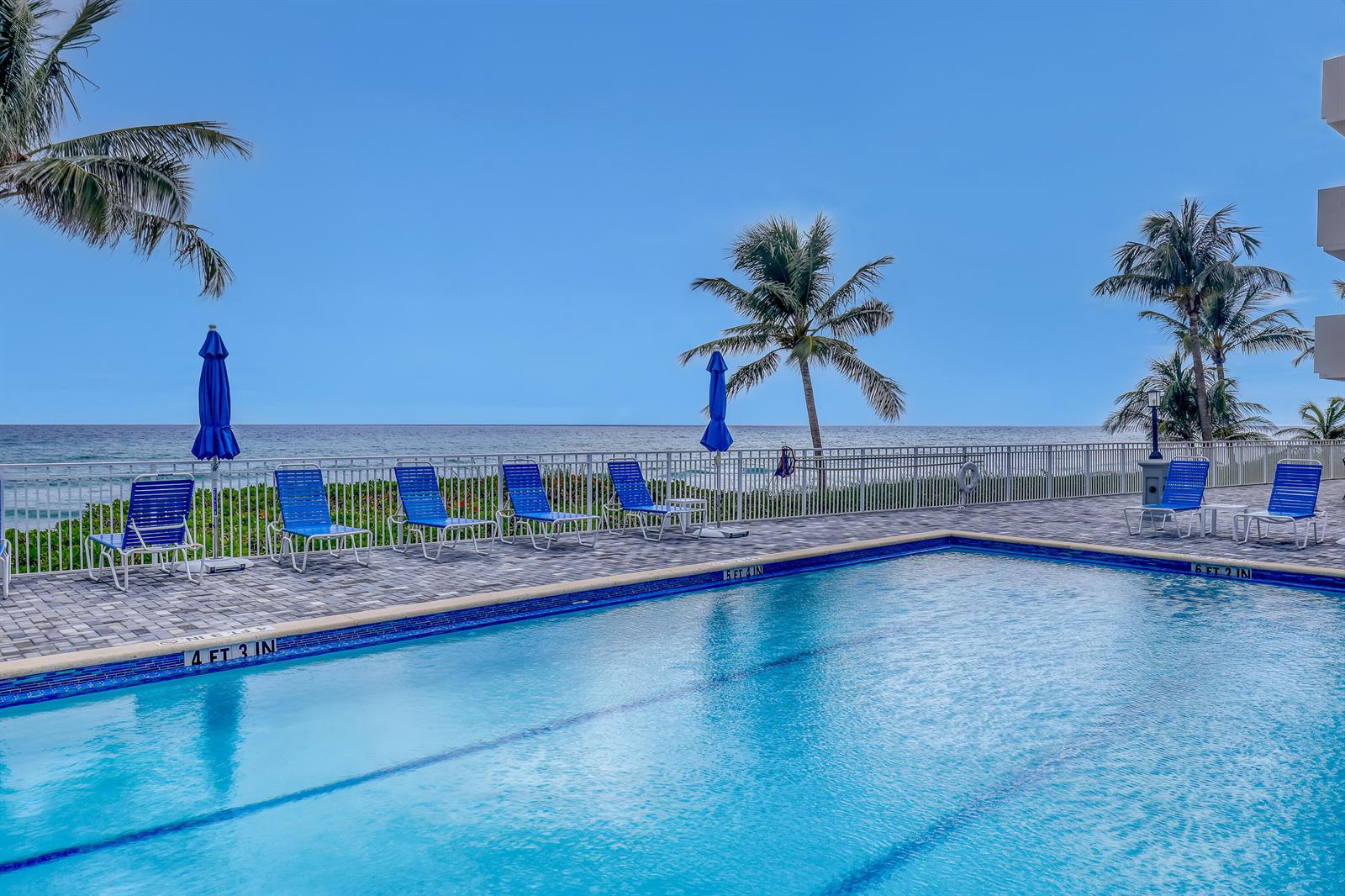 A swimming pool with lounge chairs overlooks the ocean under a clear blue sky — 3215 S Ocean Boulevard # 702, Highland Beach FL 33487, HIGHLAND BEACH, FL