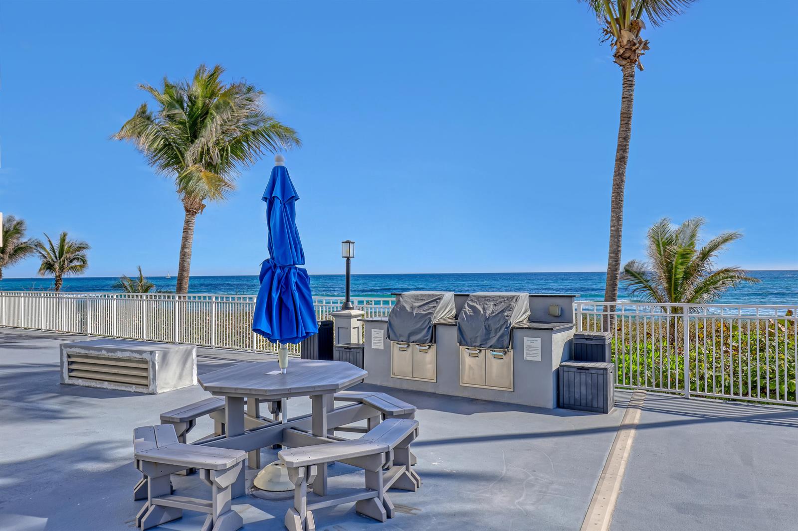 An outdoor patio features a picnic table with a blue umbrella and two covered grills — 3215 S Ocean Boulevard # 702, Highland Beach FL 33487, HIGHLAND BEACH, FL