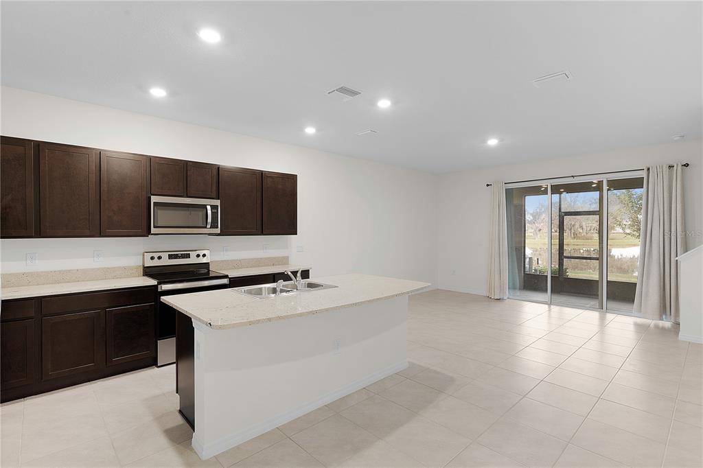 A kitchen with dark cabinets, light countertops, and an island opens to a living area — 5322 DRAGON FLY DRIVE, WILDWOOD, FL
