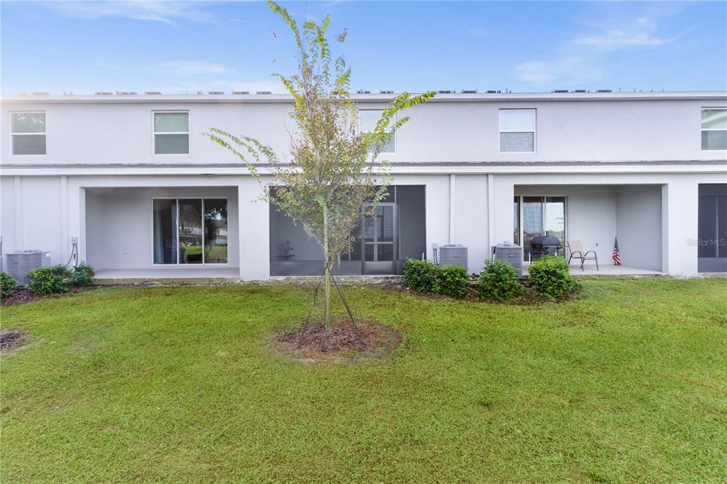The exterior rear view of a two-story townhouse features a screened patio and lawn — 5322 DRAGON FLY DRIVE, WILDWOOD, FL