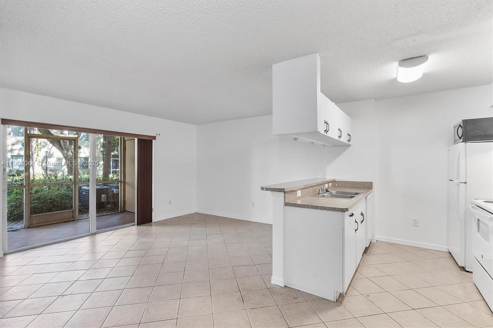 An open-concept kitchen with white cabinets and tile flooring connects to a living area — 450 S Park Rd # 105, Hollywood FL 33021, HOLLYWOOD, FL