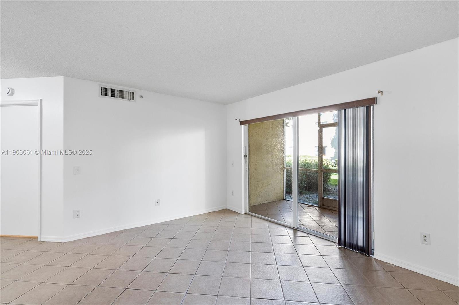 An empty room with beige tile flooring, white walls, and a sliding glass door to a patio — 450 S Park Rd # 105, Hollywood FL 33021, HOLLYWOOD, FL