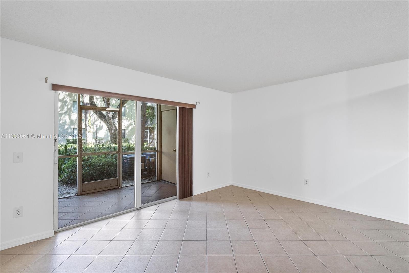 An empty room features white walls, beige tile flooring, and a sliding glass door — 450 S Park Rd # 105, Hollywood FL 33021, HOLLYWOOD, FL