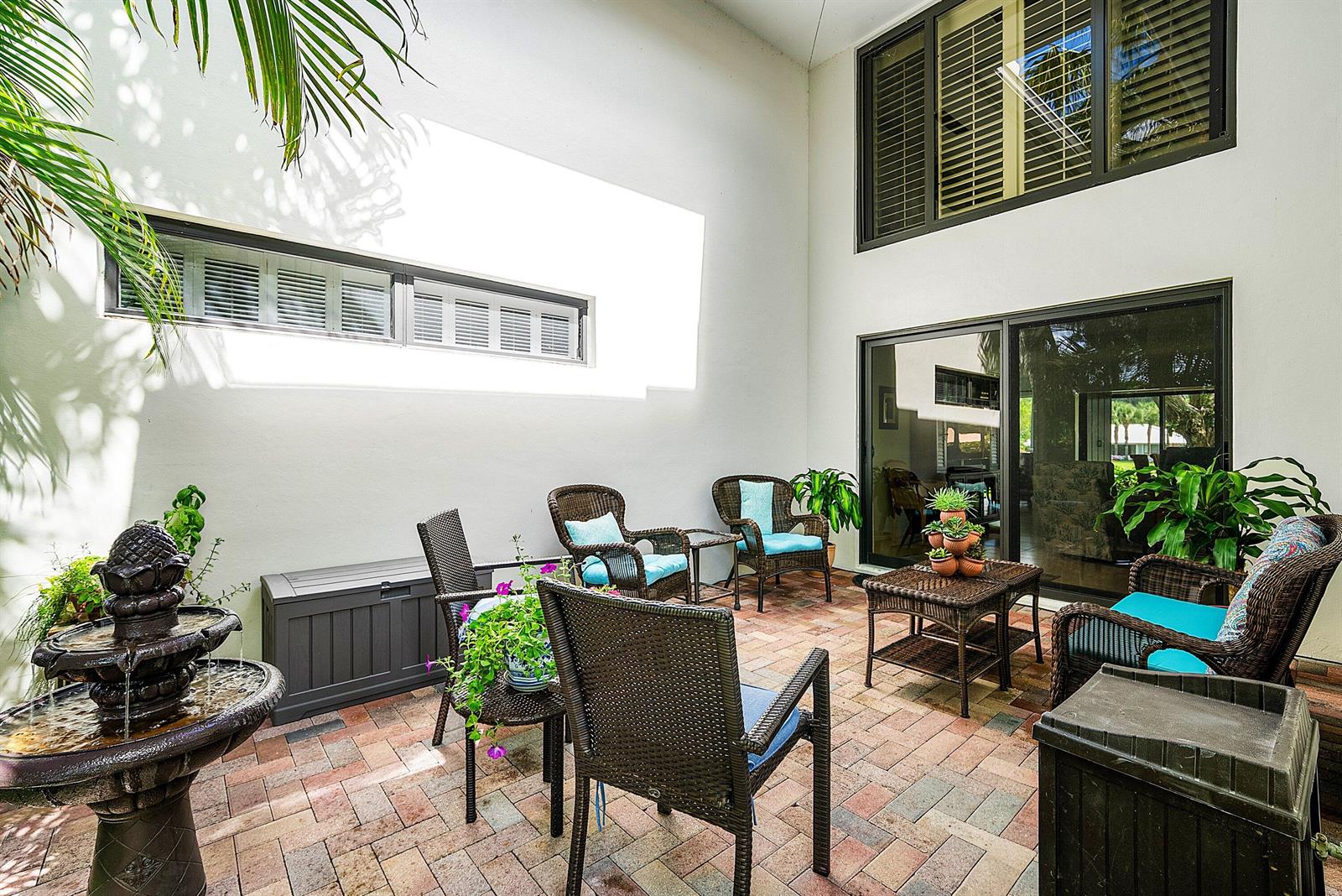 A paved outdoor patio features wicker furniture, a tiered water fountain, and large sliding doors — 3682 Quail Ridge Drive N, Boynton Beach FL 33436, BOYNTON BEACH, FL