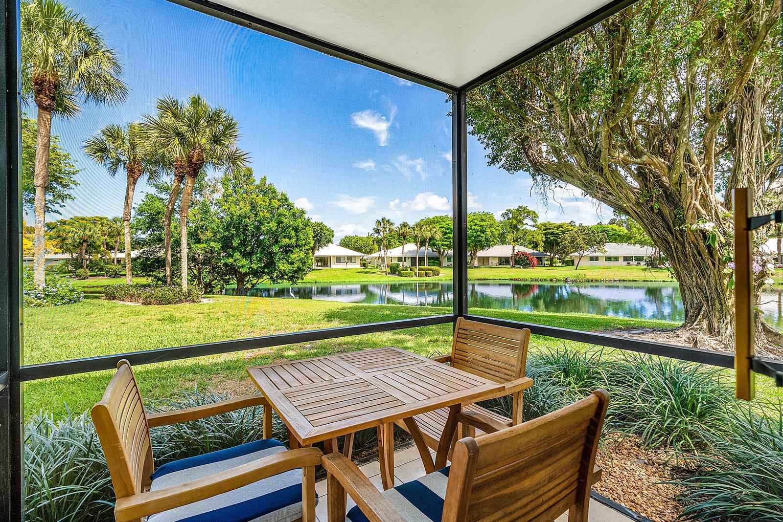A screened-in patio features a wooden dining set overlooking a pond and palm trees — 3682 Quail Ridge Drive N, Boynton Beach FL 33436, BOYNTON BEACH, FL